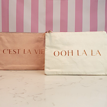 Load image into Gallery viewer, A pink makeup bag with &quot;C&#39;est la vie&quot; slogan and a cream coloured makeup bag with an &quot;ooh la la&quot; slogan
